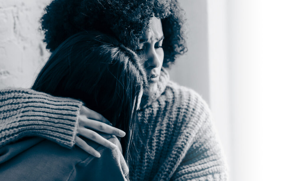 Two women hugging indoors, providing emotional support and comfort in a cozy setting.